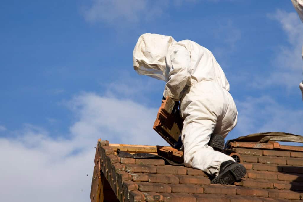 Construction worker in a white protective suit atop a wooden roof against a blue sky.